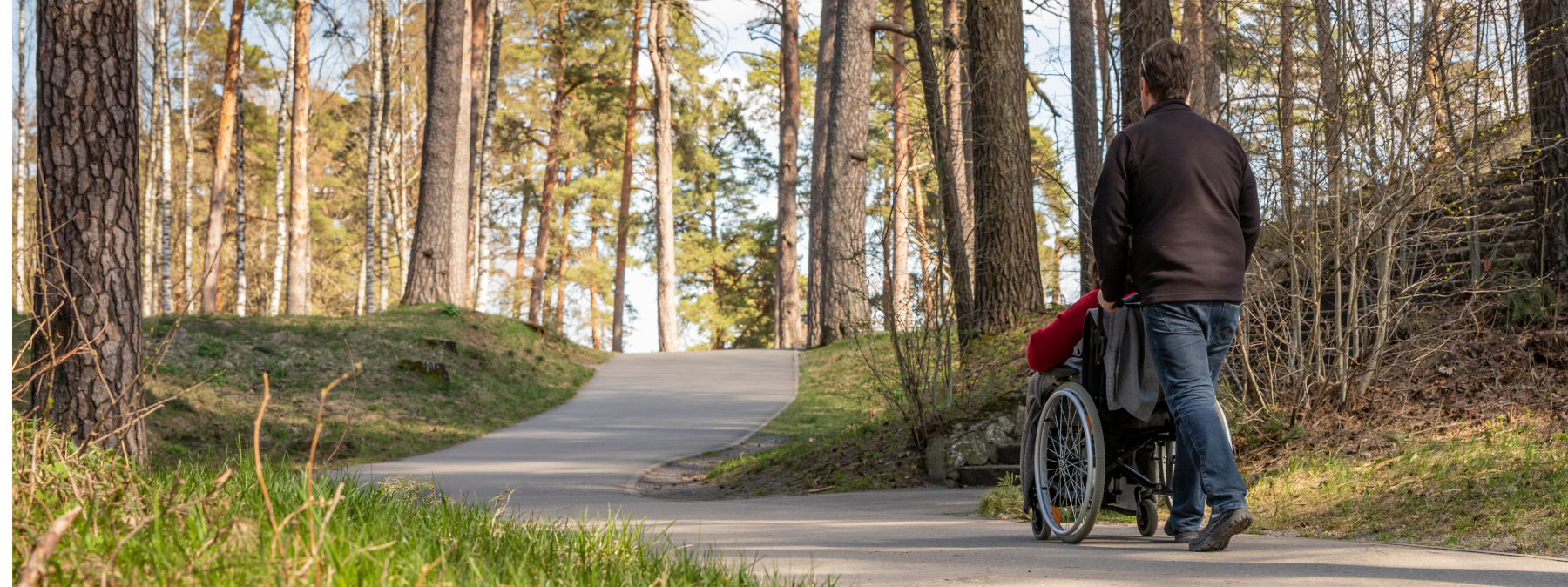 Person in wheelchair and a helper having relaxing walk on curvy park path