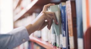 a hand picking out a book on a shelf