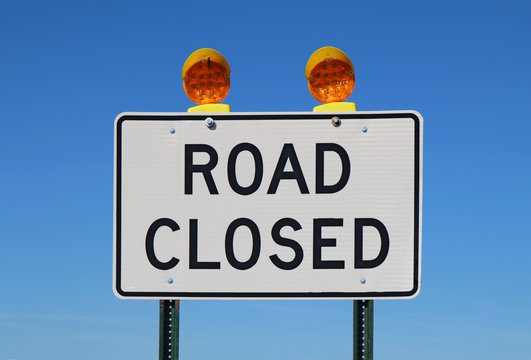 white road closed sign with lights on top